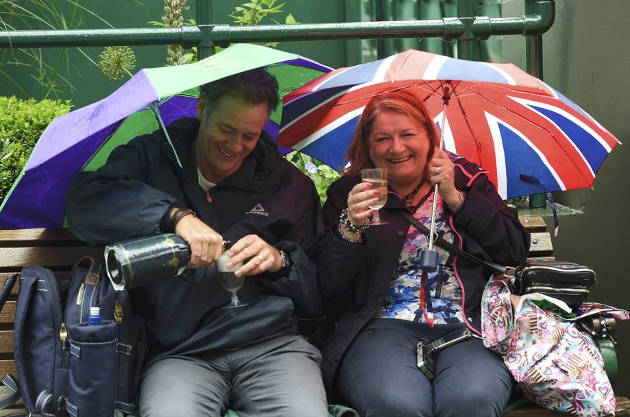 Ricominica a piovere sui campi di Wimbledon, due spettatori si consolano con un brindisi (Reuters)